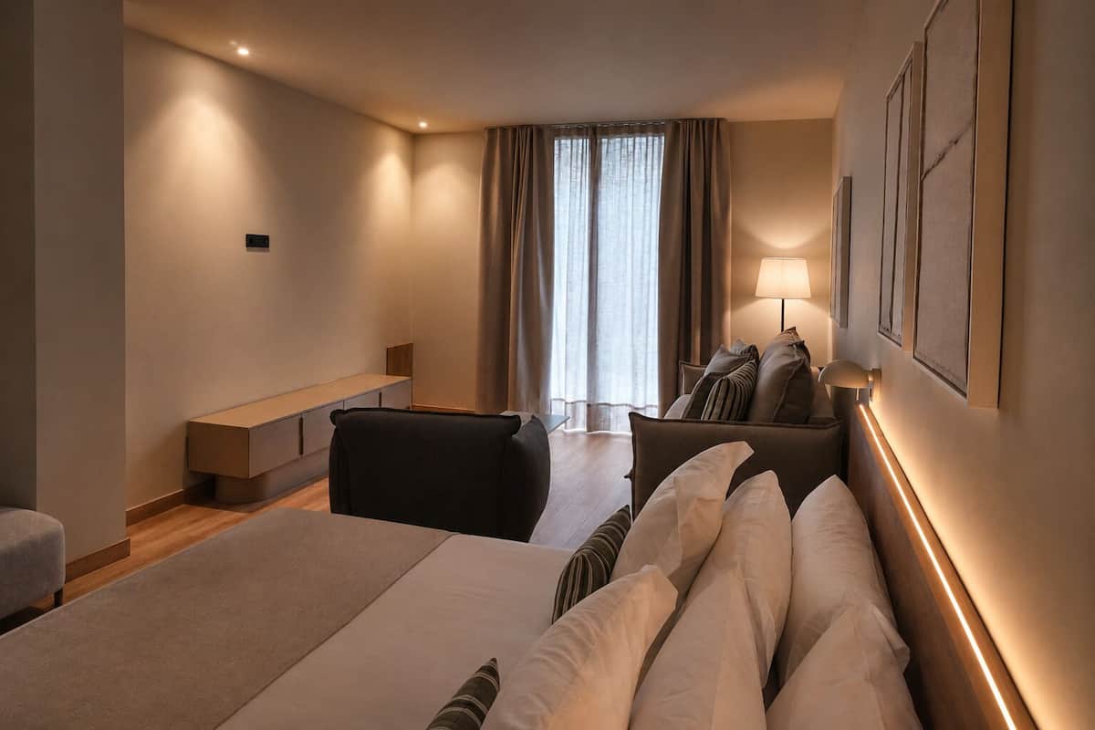A modern hotel room with a bed, a sofa, a desk, and a window with curtains.