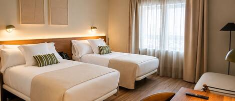 Quarto de hotel com duas camas, piso de madeira, escrivaninha e luminária.