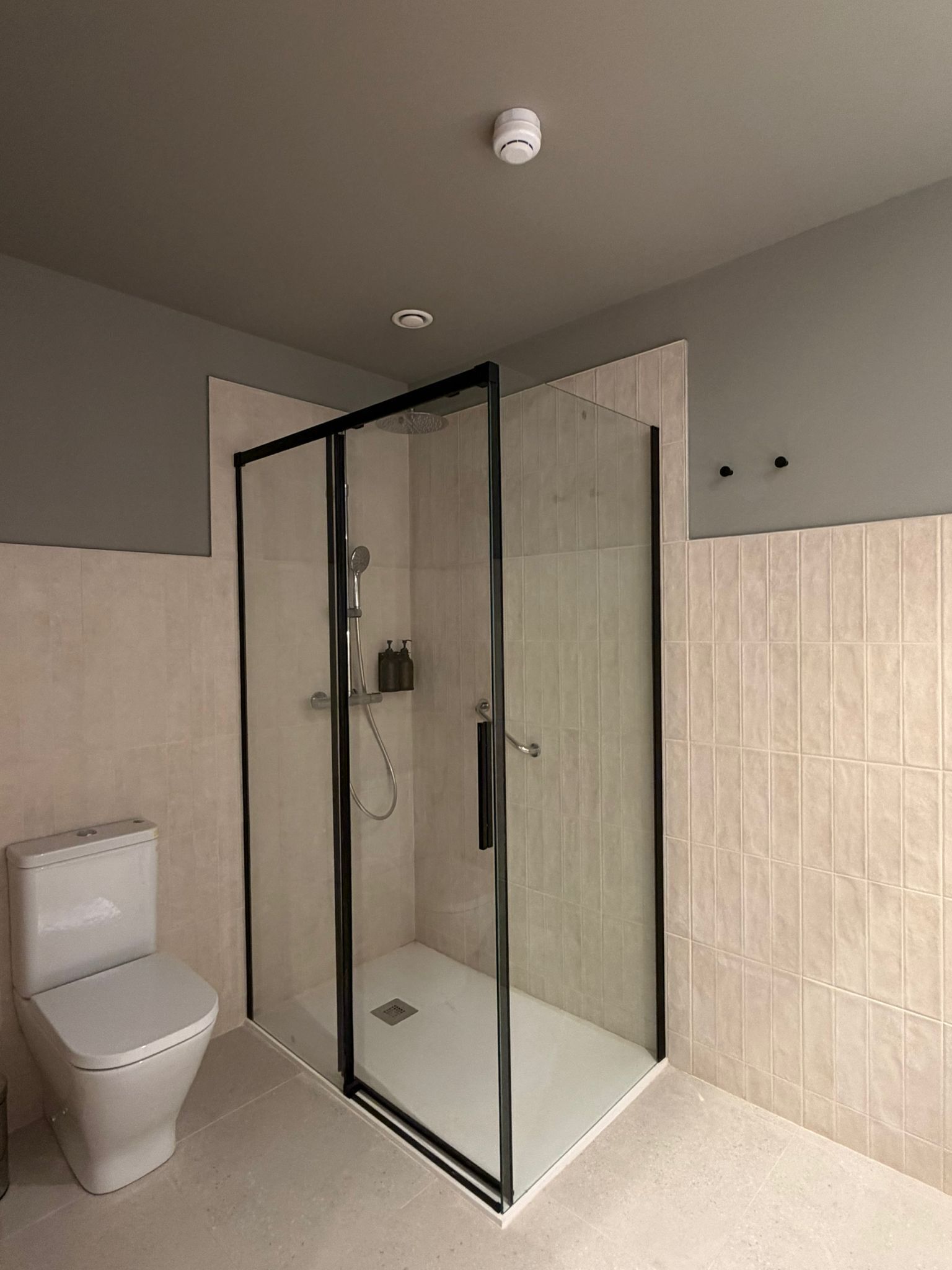 Et moderne badeværelse med en glasafskærmet brusekabine, toilet og flisebeklædte vægge.