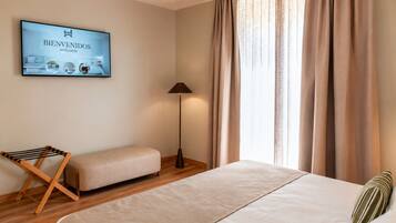Una habitación de hotel con cama, un banco, una lámpara de pie y un cartel de bienvenida.