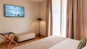 A hotel room with a bed, a bench, a floor lamp, and a welcome sign.
