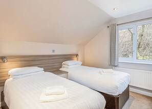 A hotel room with two beds, a window with curtains, and a radiator. - Ocean Breeze Villa 3 Hot Tub (Woolacombe)