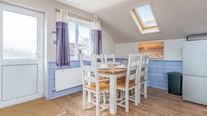 Een keuken met een eettafel, stoelen, een koelkast en een raam met gordijnen.