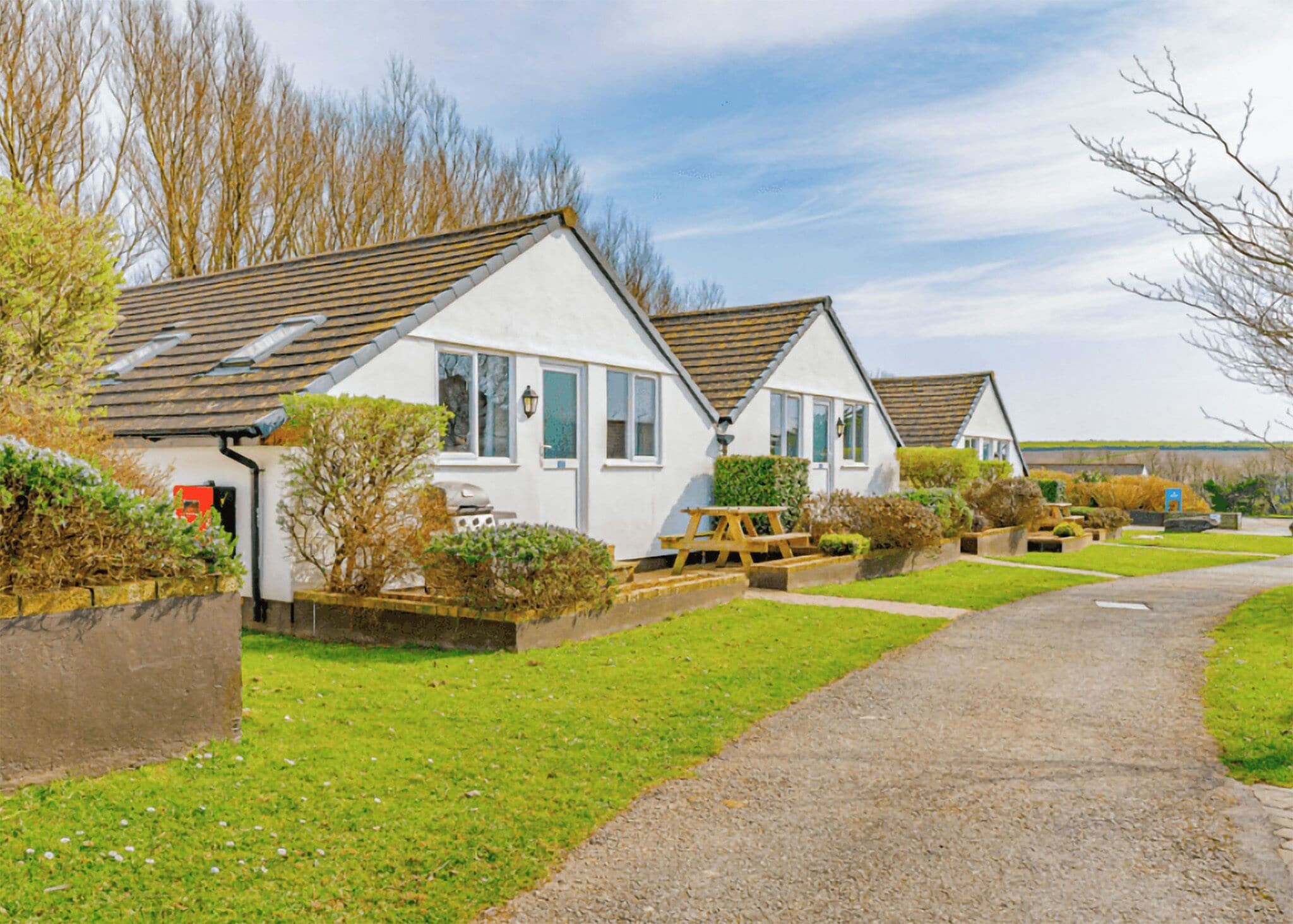 A row of white cottages with pitched roofs, a gravel path, and a grassy lawn.
