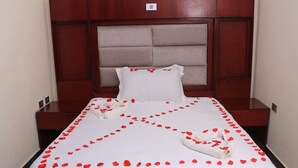 A neatly made bed with rose petals arranged on the bedspread, a wooden headboard, and a small rug on the floor. - Yemata Hotel (Gondar)