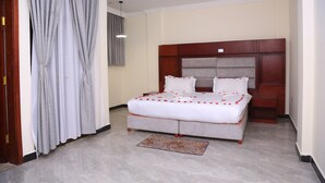 A bedroom with a large bed, a wooden headboard, and a small bedside table. - Yemata Hotel (Gondar)