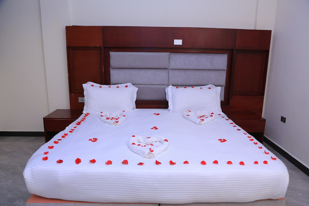 A neatly made bed with white linens, a wooden headboard, and red rose petals arranged on the bed.