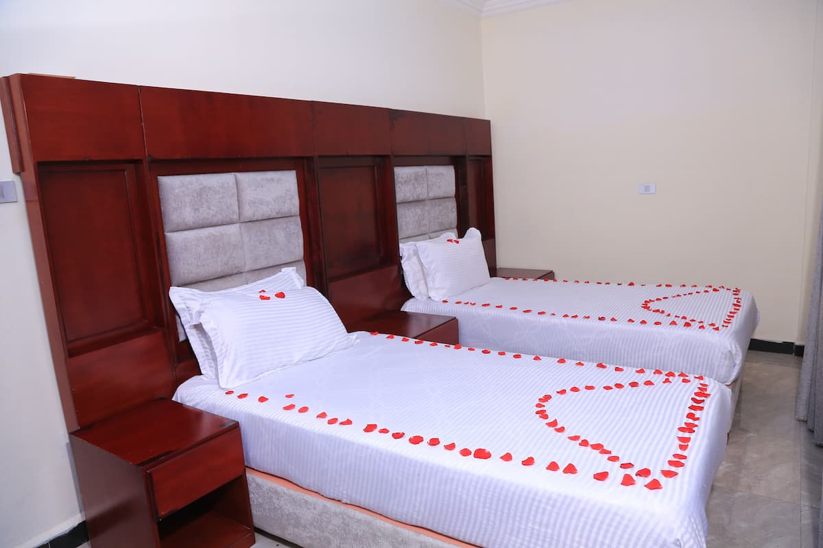 Two single beds with wooden headboards and white bedding, arranged in a room with a tiled floor.