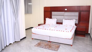 A neatly made bed with a white comforter and red accents, a wooden headboard, and a small bedside table. - Yemata Hotel (Gondar)