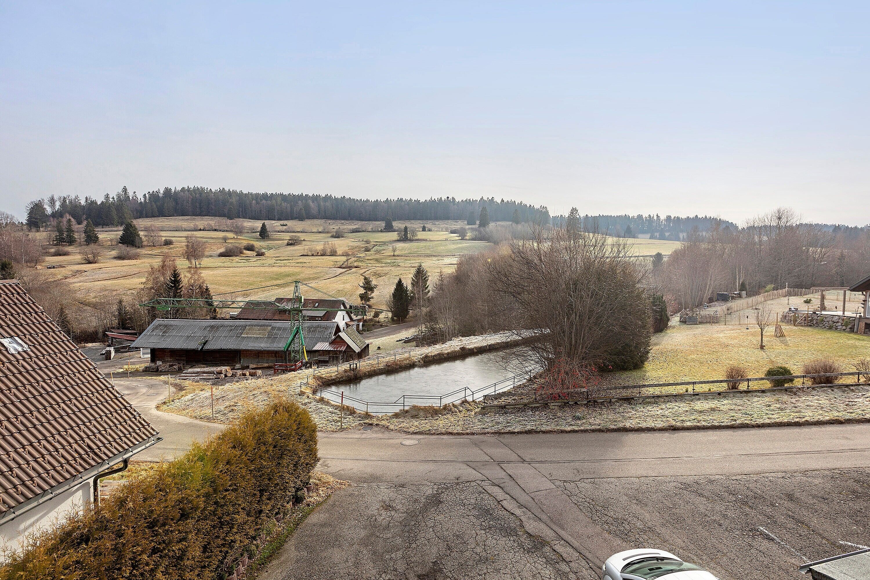 Paisagem rural com um lago, uma estrada e um edifício com telhado de telhas.