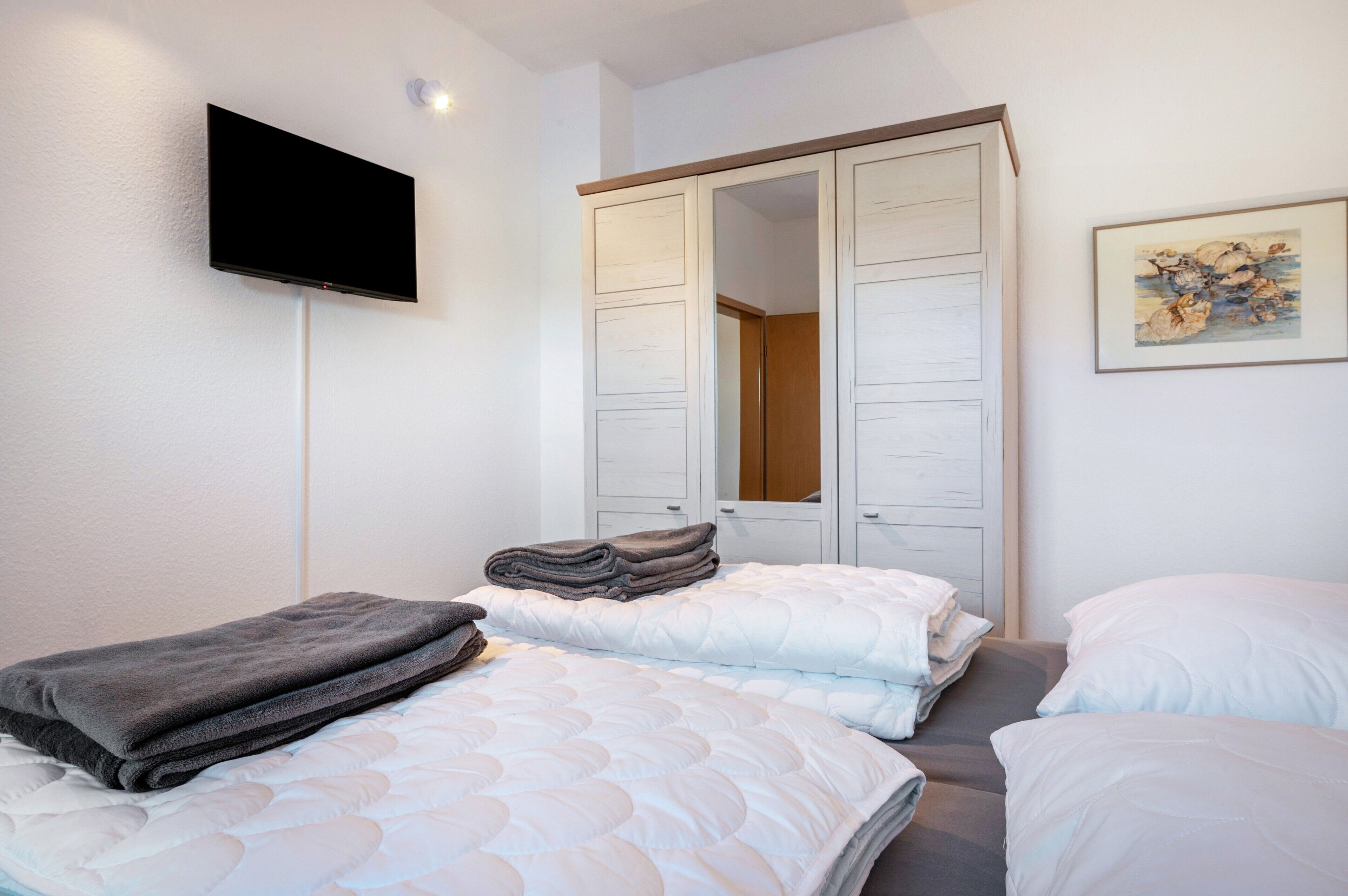 A bedroom with a bed, a TV mounted on the wall, a wardrobe, and a painting.