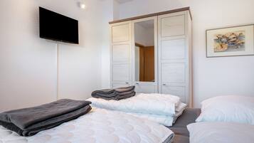 A bedroom with a bed, a TV mounted on the wall, a wardrobe, and a painting.