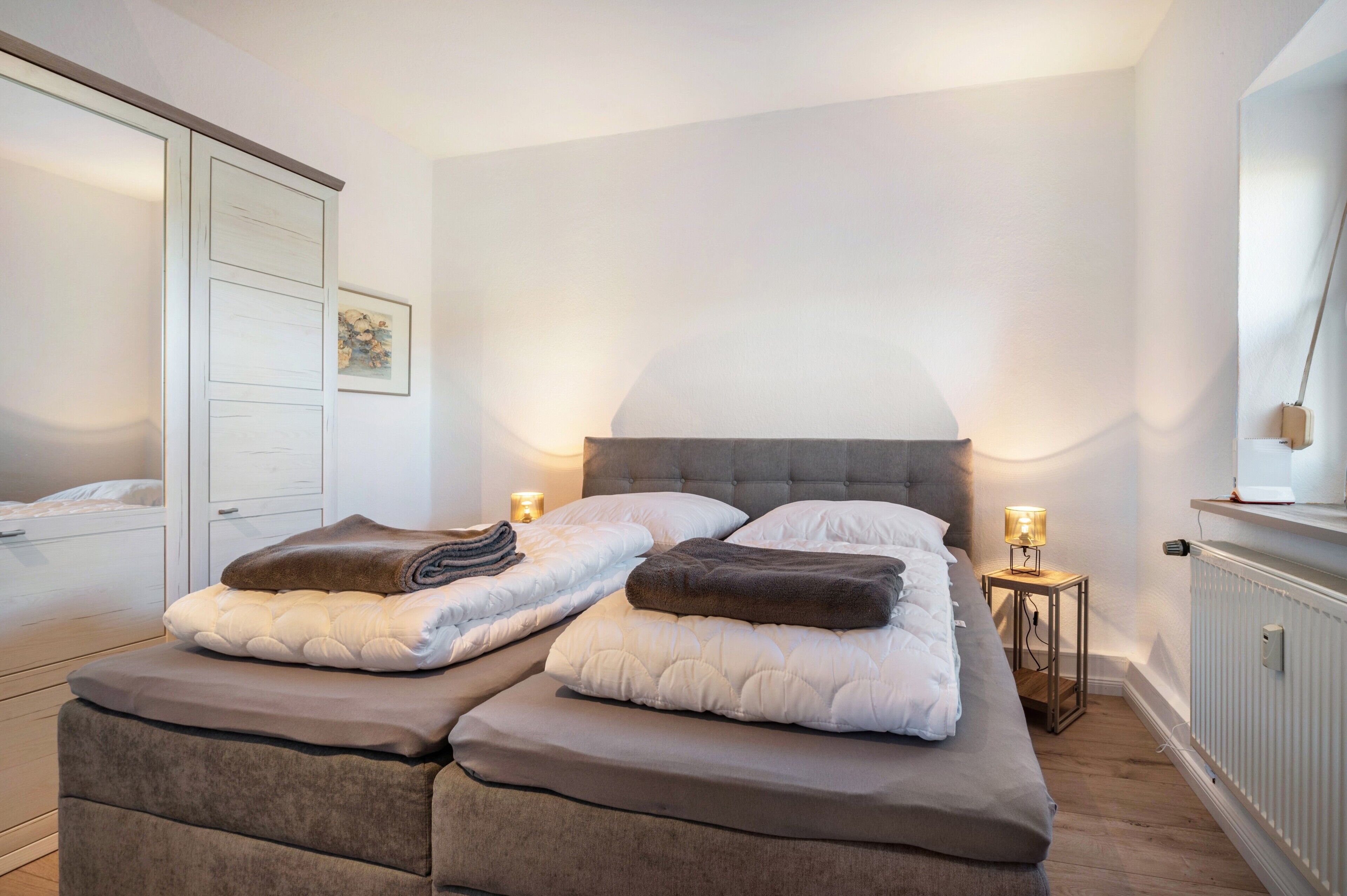 Ein Schlafzimmer mit einem großen Bett, zwei Nachttischen mit Lampen, einem Kleiderschrank und einer Heizung.