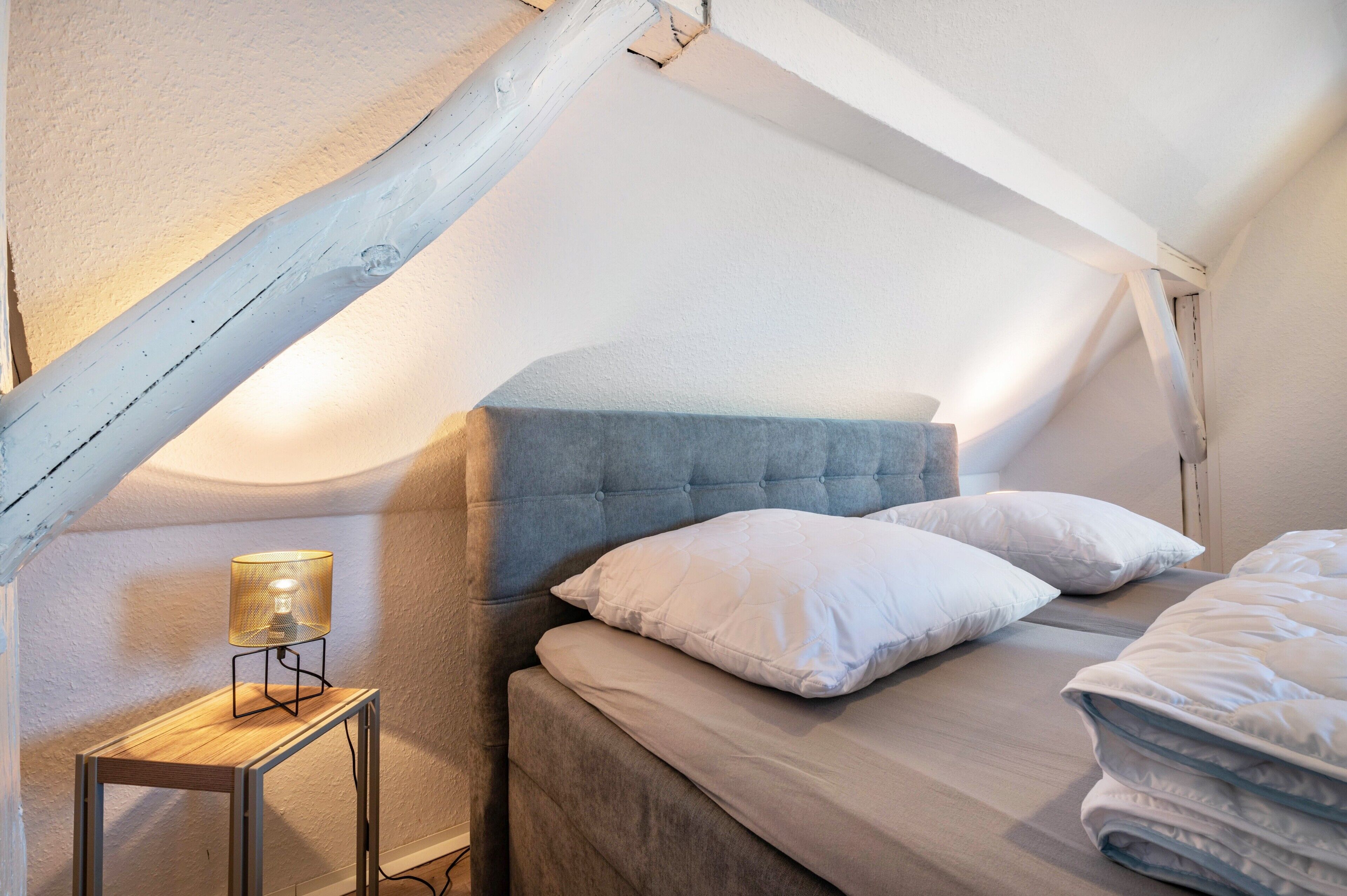 Een slaapkamer met een bed, kussens, een bedlampje en een nachtkastje van hout.