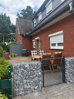 Ein Backsteinhaus mit einer Terrasse, einem Tisch, Stühlen und einem Tor.