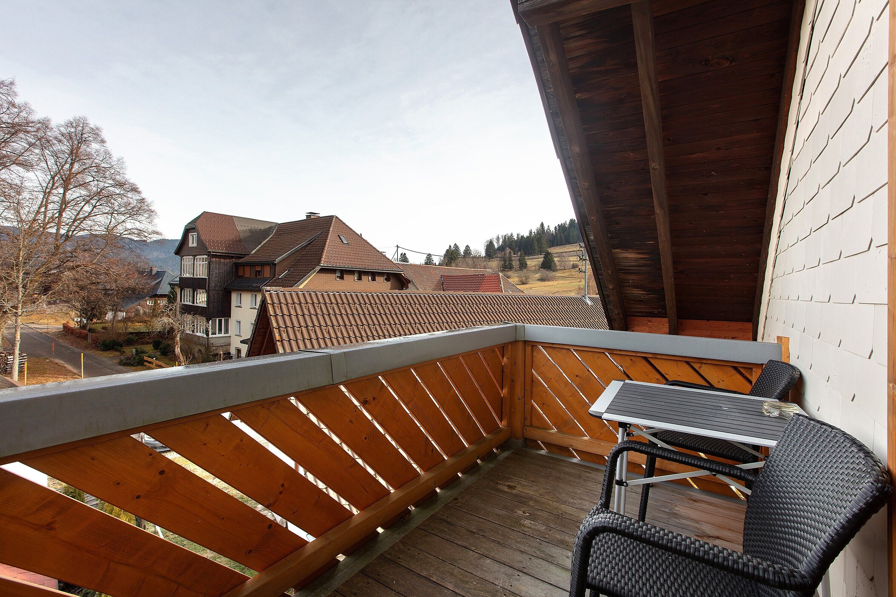 A wooden deck with a table and chairs, overlooking a residential area with houses and trees.