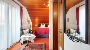 A hotel room with a bed, a table with a tray, a chair, a mirror, and a red carpet. - Hotel Bären – Drei Sterne: Doppelzimmer 8 inkl. Frühstück, Balkon, Bergblick, WLAN (Bernau im Schwarzwald)