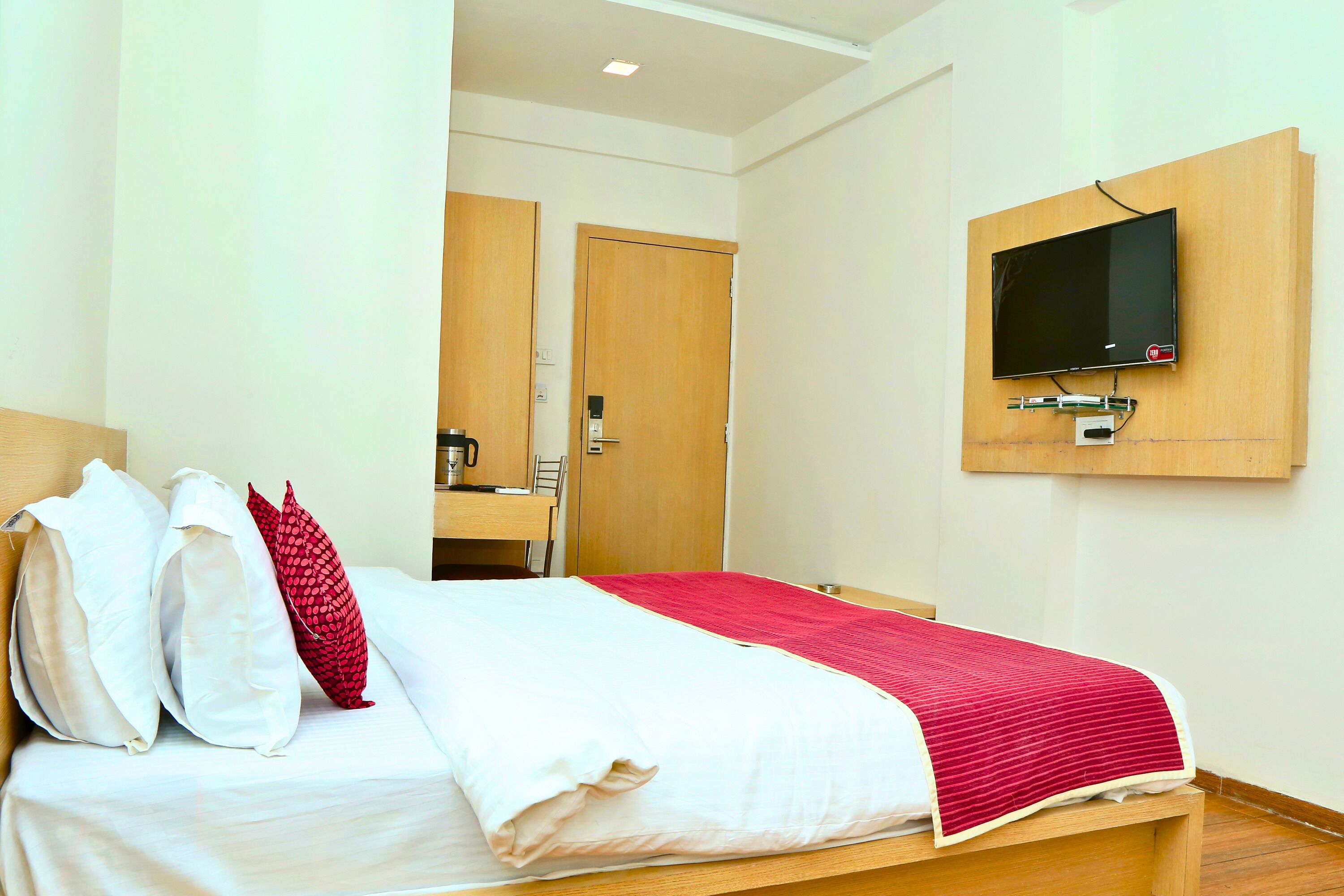 Een hotelkamer met een bed, een aan de muur bevestigde televisie en een houten bureau met stoel.