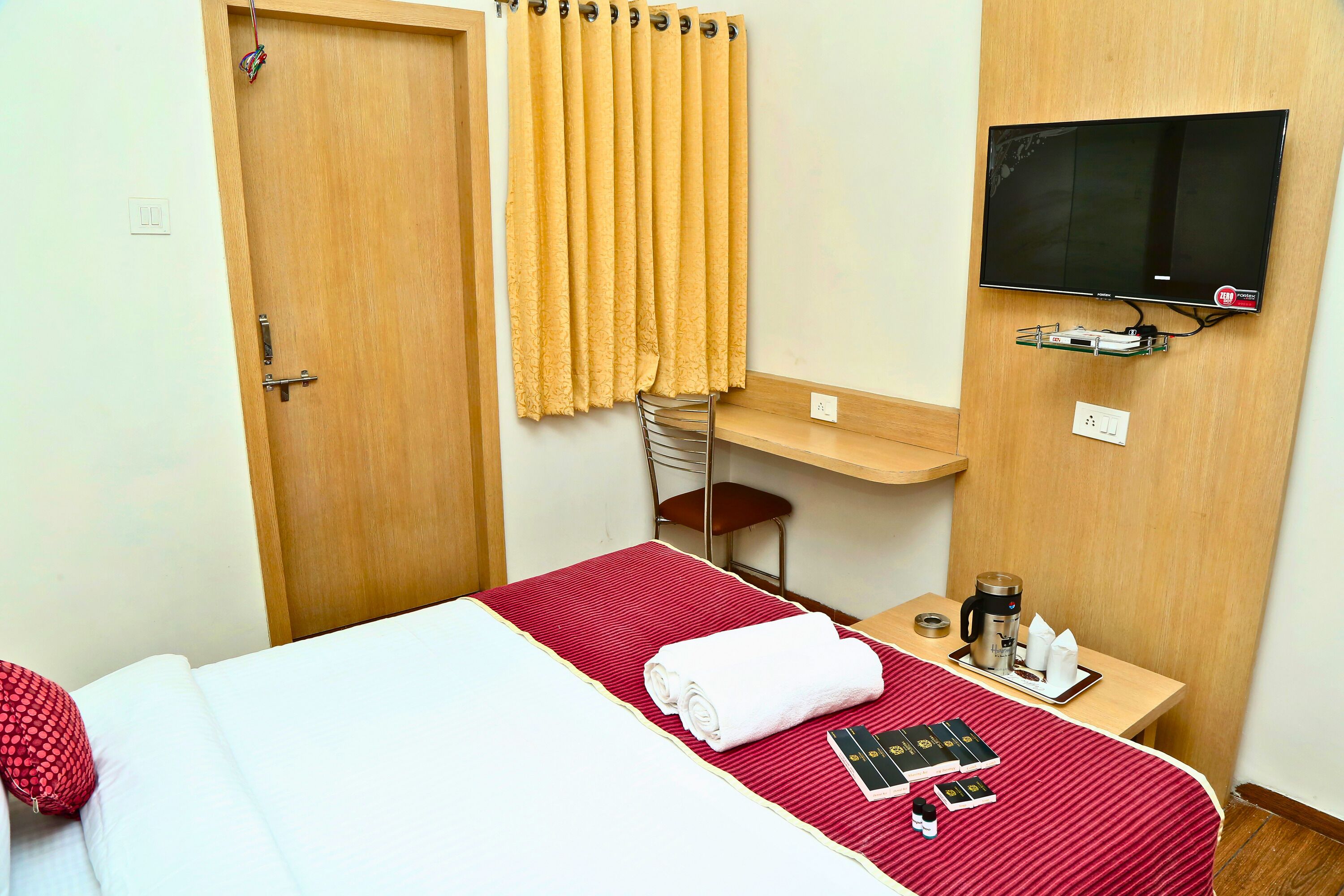 A hotel room with a bed, a TV, a desk with a chair, and a small table with a coffee maker and books.