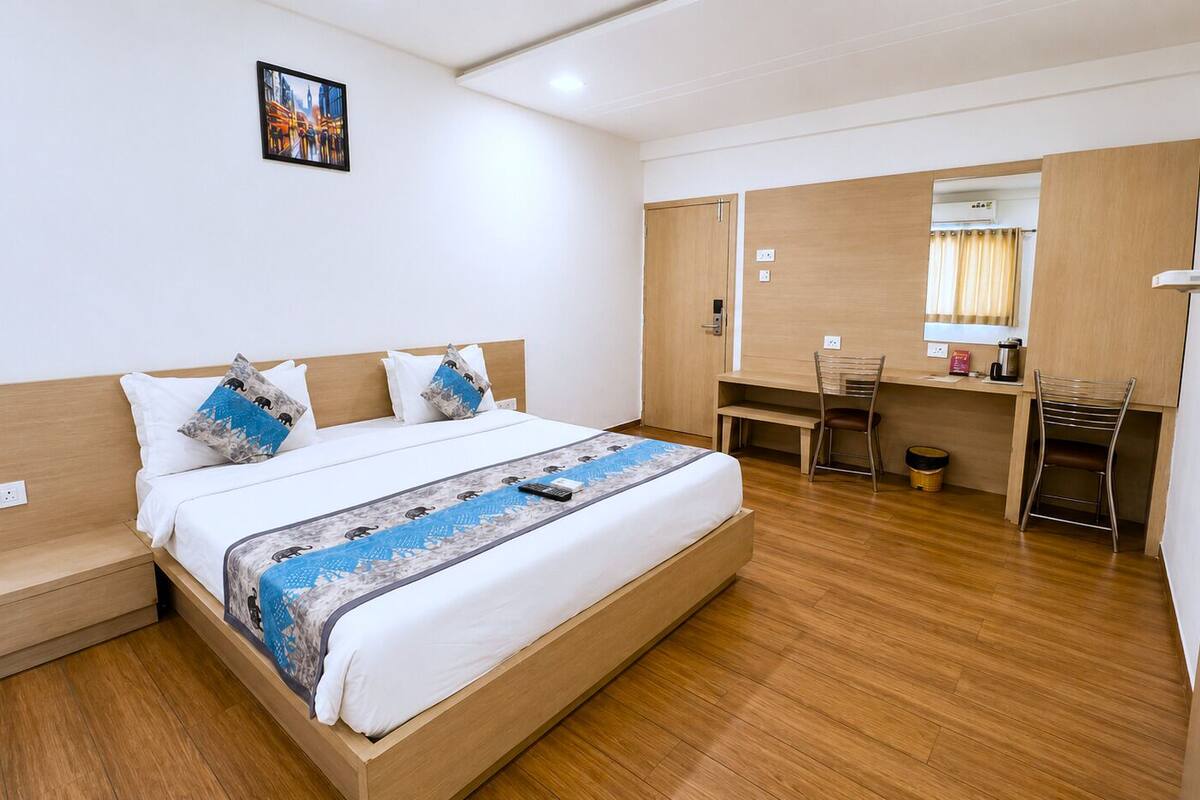 A hotel room with a bed, a desk, a chair, a TV, and a small bathroom area.