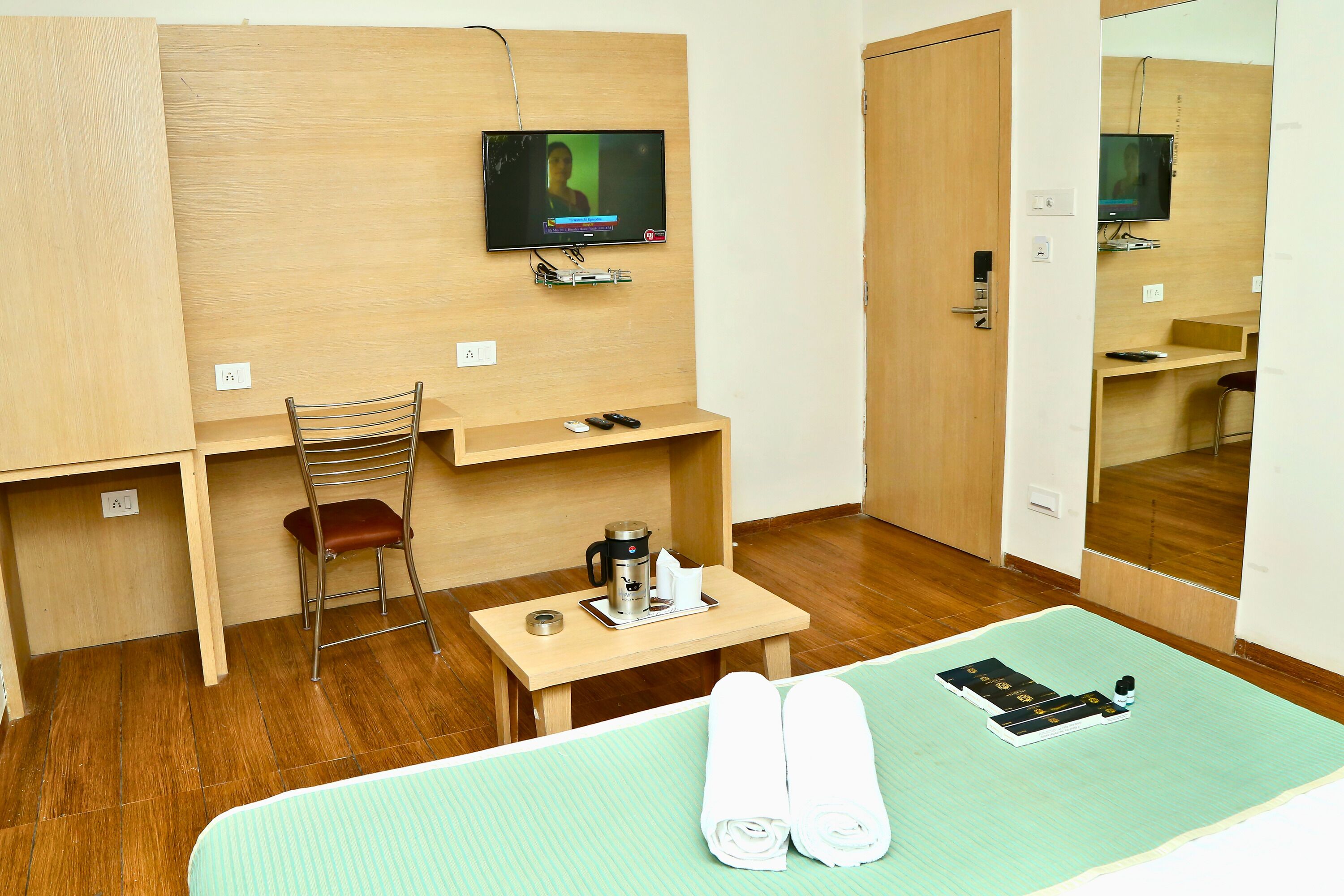 Una habitación de hotel con cama, escritorio, silla, televisor y espejo.