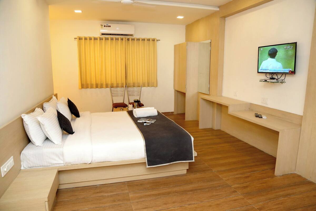 A hotel room with a bed, a TV mounted on the wall, a mirror, and a small shelf.