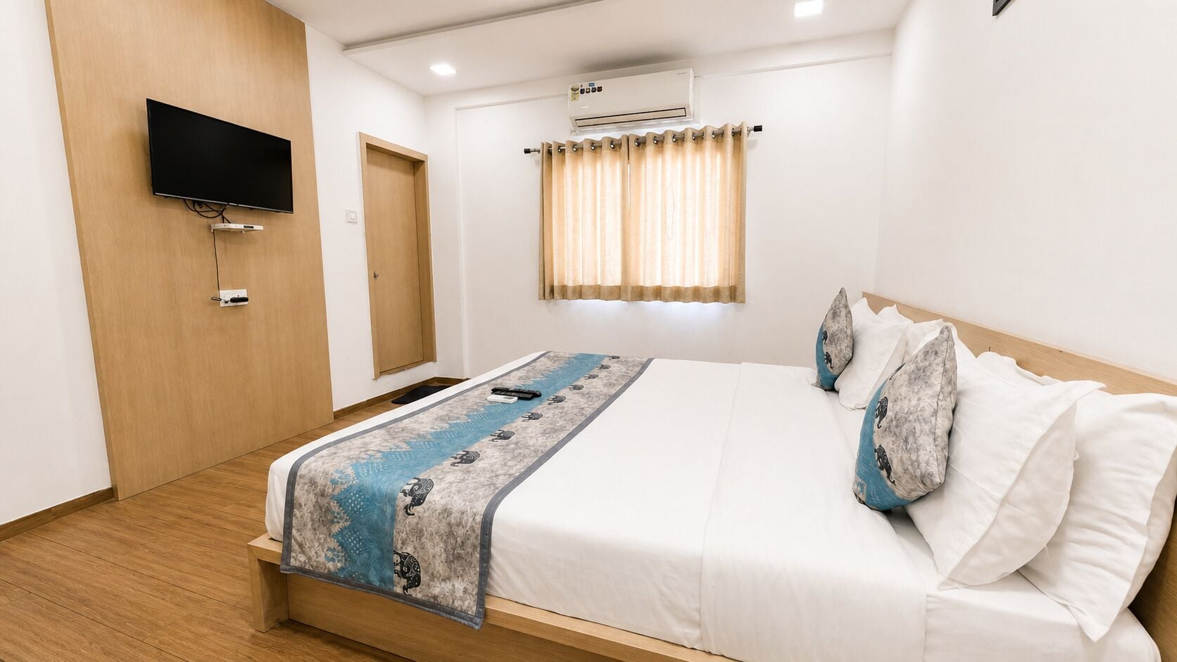 Una camera d'albergo moderna con un letto, una TV a schermo piatto montata a parete, una finestra con tende e un condizionatore.