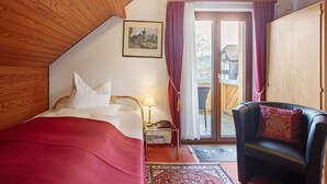 A bedroom with a bed, a chair, a nightstand with a lamp, and a door leading to a balcony. - Hotel Bären – Three-Star: Single Room 9 / Breakfast Included / 1 Person / Balcony / WiFi (Bernau im Schwarzwald)