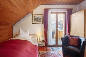 A bedroom with a bed, a chair, a nightstand with a lamp, and a door leading to a balcony. - Hotel Bären – Three-Star: Single Room 9 / Breakfast Included / 1 Person / Balcony / WiFi (Bernau im Schwarzwald)