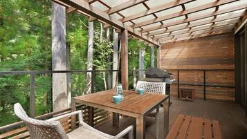 A wooden deck with a table and chairs, a grill, and a view of a forest.