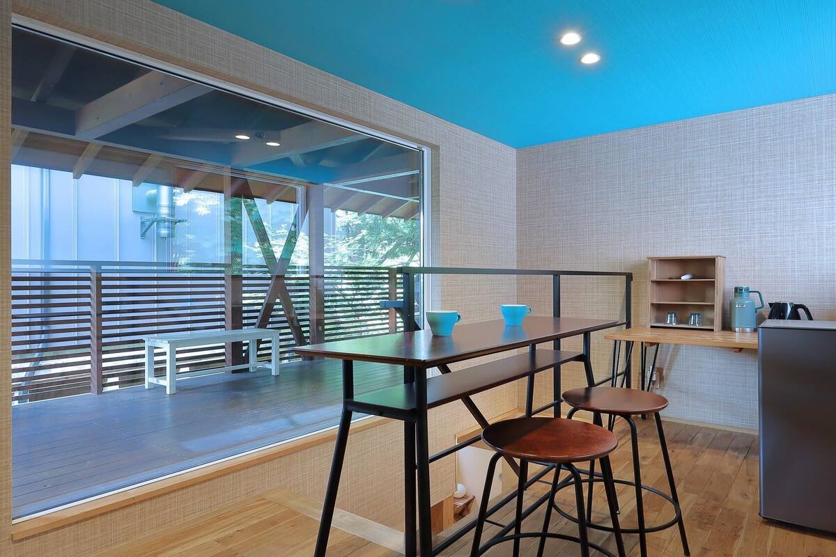 Una cocina moderna con una mesa de madera, dos taburetes, una estantería empotrada y un refrigerador.