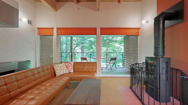 A modern living room with a leather sofa, a fireplace, and a balcony with outdoor seating. - Onsen Glamping ShimaBlue (Nakanojo)