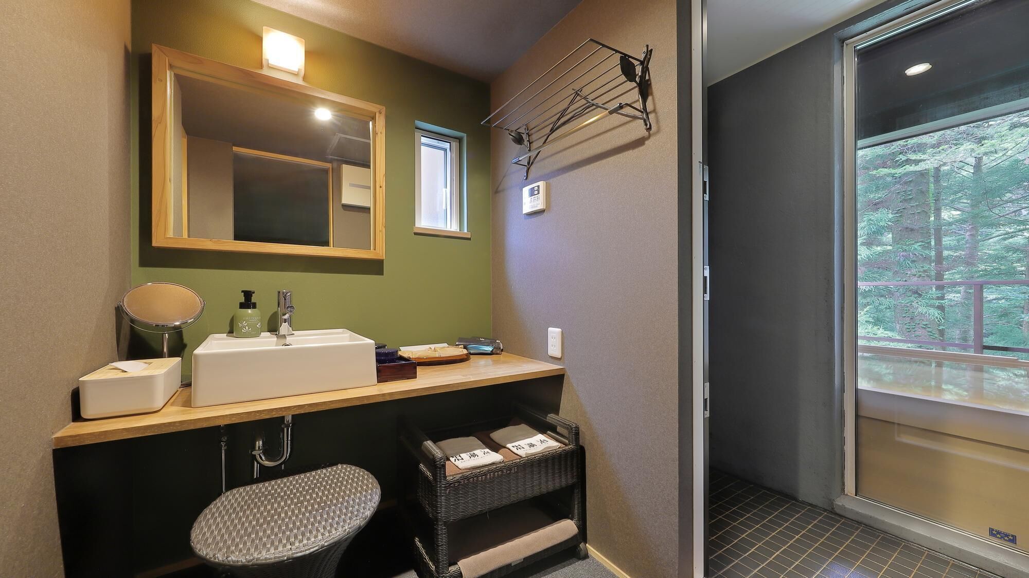 Un baño con lavamanos, espejo y ventana con vistas a árboles.