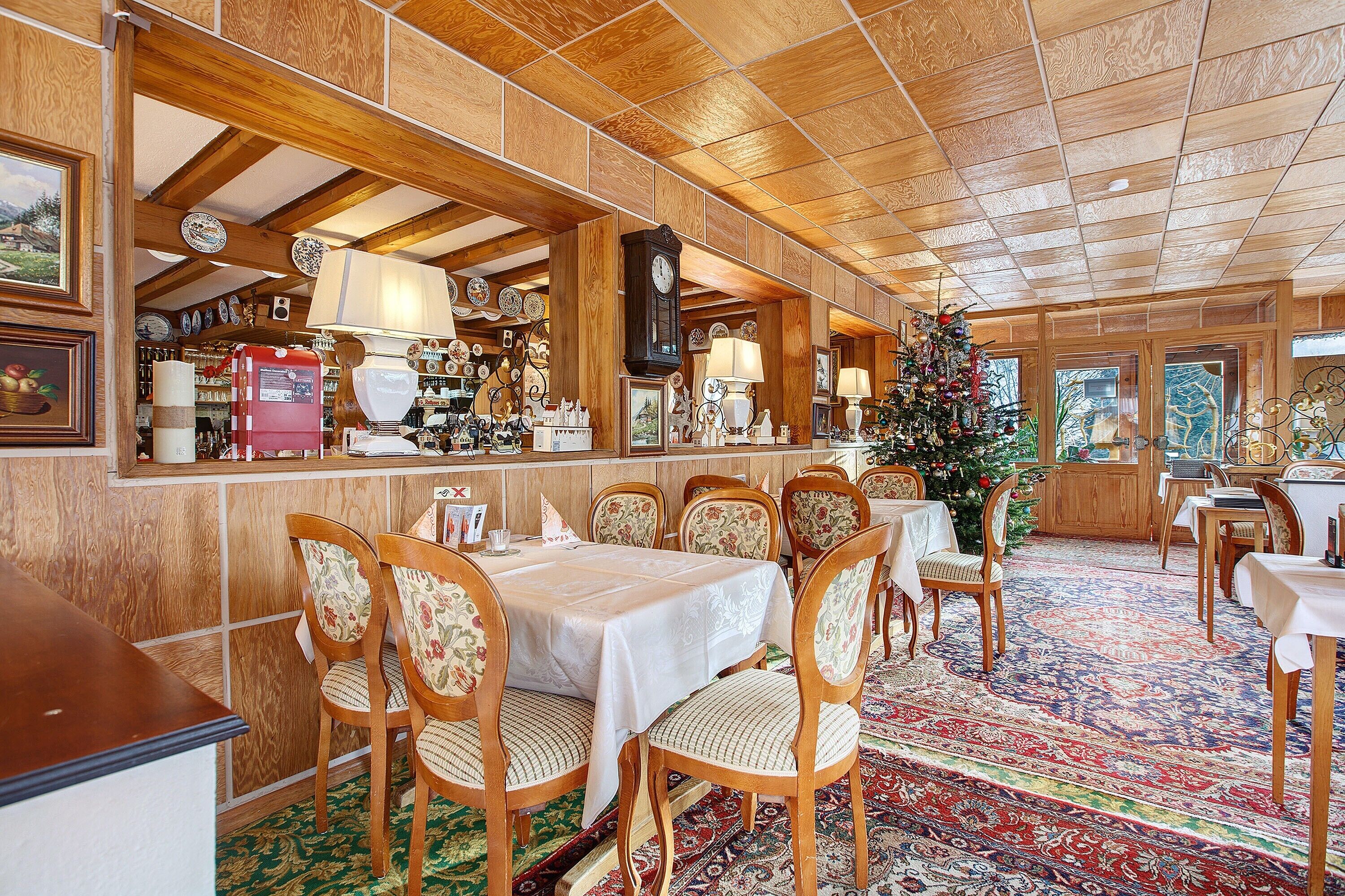 Una posada tradicional con paneles de madera, un comedor central con un árbol de Navidad y un reloj en la pared.