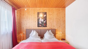 A hotel room with a wooden paneled wall, a bed with white bedding, two bedside lamps, and a painting of flowers.