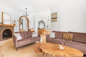 A living room with a fireplace, two sofas, a wooden coffee table, and a dining area in the background.