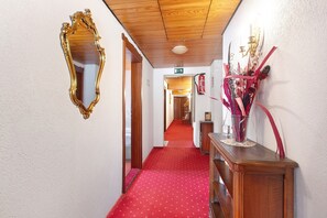 A hallway with a red carpet, a wooden ceiling, a gold-framed mirror, and a decorative vase on a wooden console. - Hotel Bären - Three Stars: Single Room 11 / Breakfast Included / 1 Person / WiFi (Bernau im Schwarzwald)