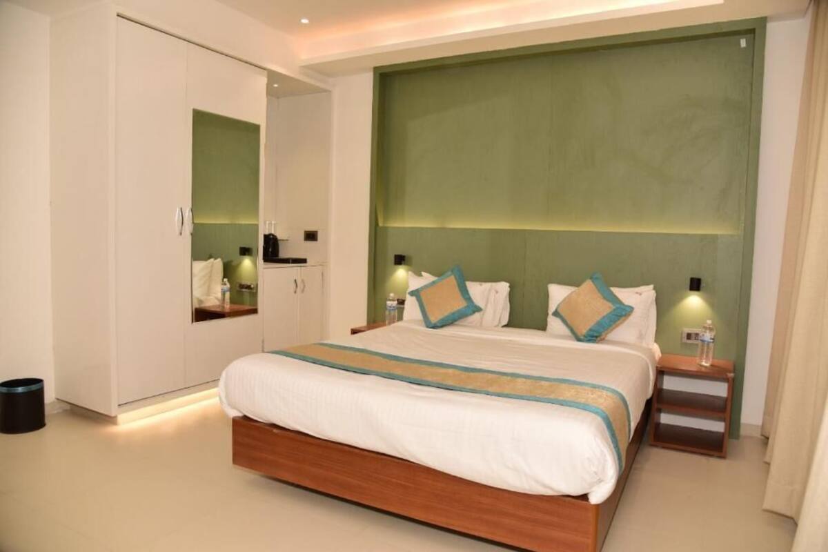 A modern hotel room with a large bed, a wardrobe, a bedside table, and a green accent wall.