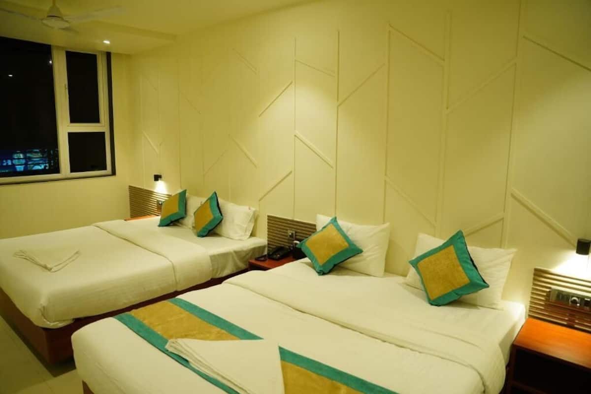 A hotel room with two single beds, a nightstand, a lamp, and a window with blinds.