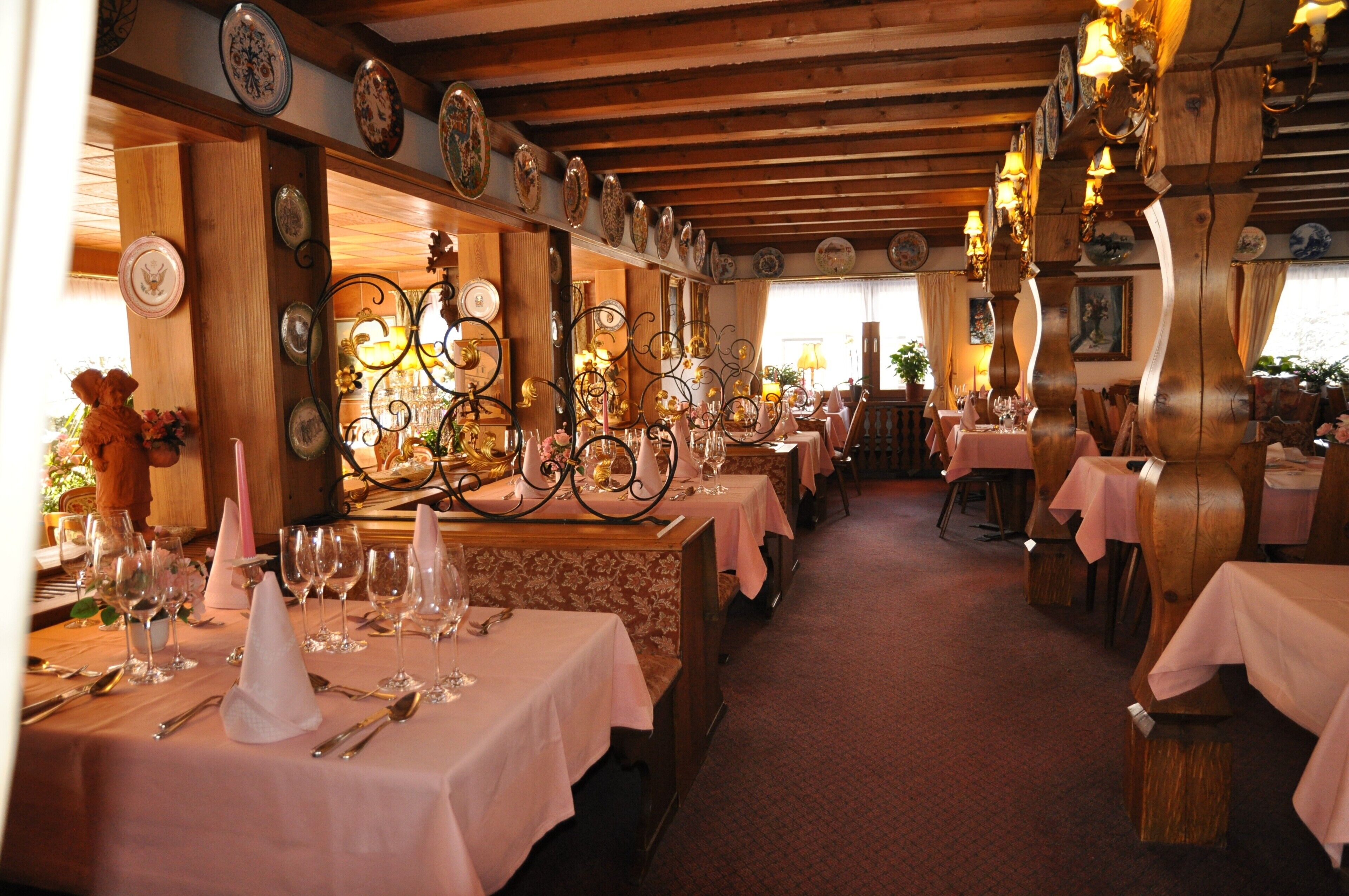 Un restaurant avec de nombreuses tables dressées pour le service, des poutres en bois au plafond et des assiettes décoratives accrochées aux murs.
