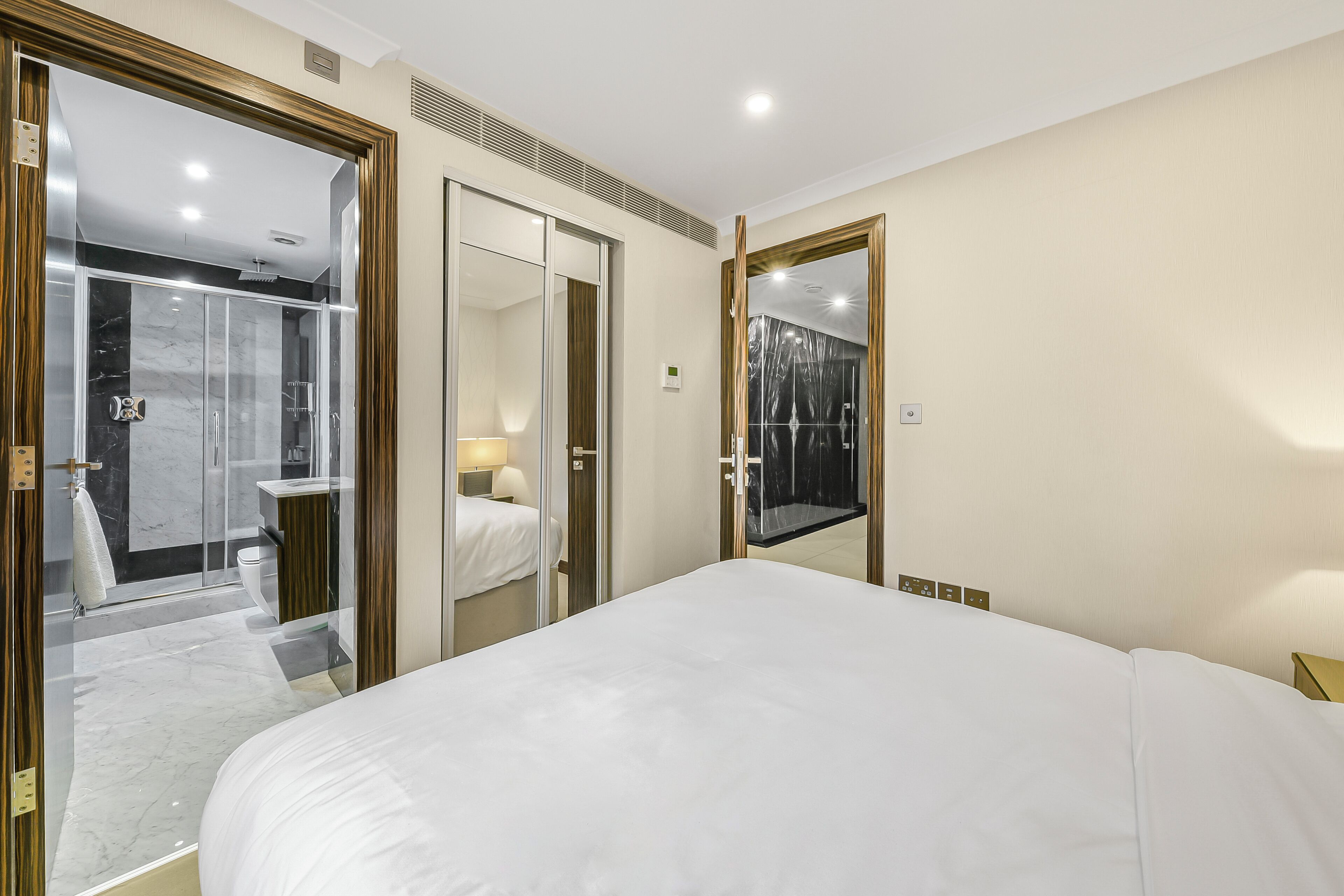 A modern hotel room with a large bed, a glass-enclosed shower area, and a mirror reflecting the room.
