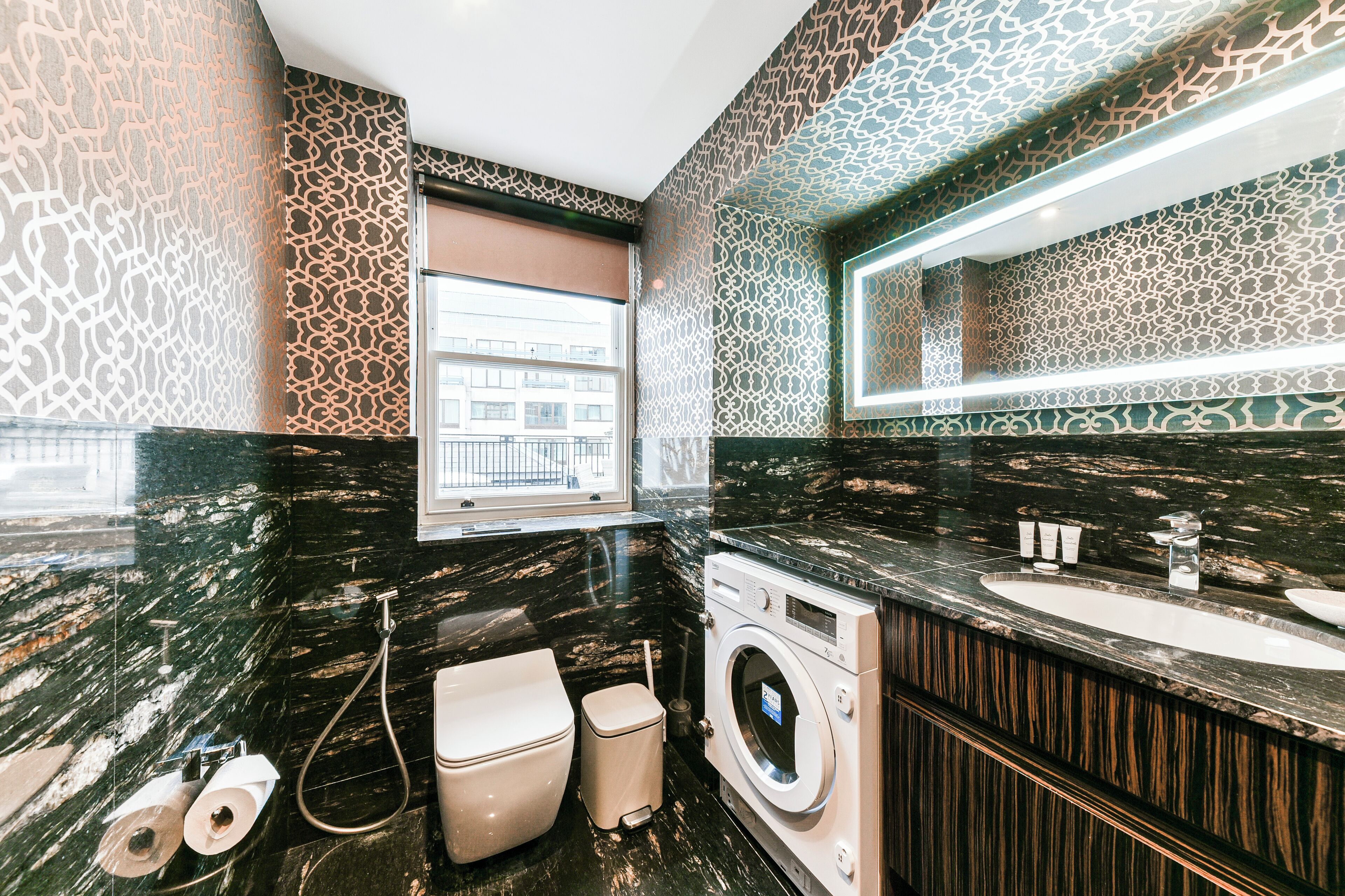 A modern bathroom with a black marble countertop, a built-in washing machine, and a large mirror.