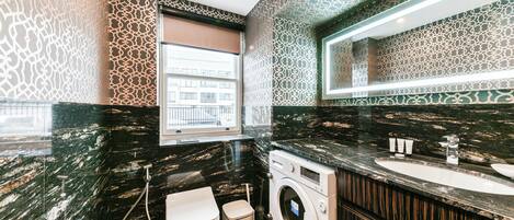 A modern bathroom with a black marble countertop, a built-in washing machine, and a large mirror.