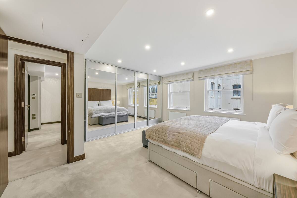 Ein Schlafzimmer mit einem großen Bett, einem Kleiderschrank, einem Spiegel und einem Fenster.