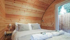 Um quarto de cabana aconchegante, com decoração em madeira, uma cama com travesseiros fofos, uma mesa de cabeceira com abajur e uma janela com vista para árvores.
