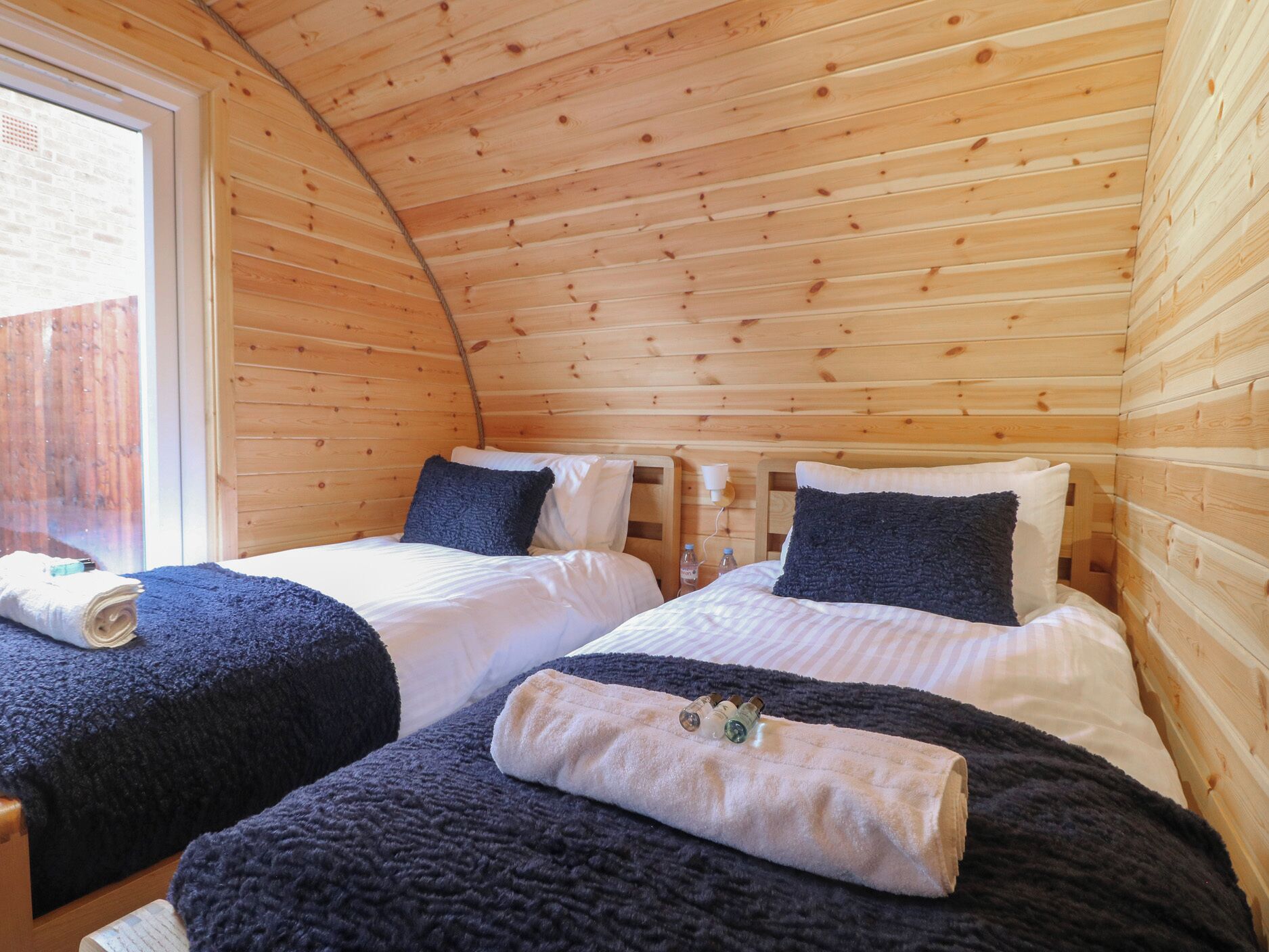 Habitació d'una cabana acollidora, amb dos llits, parets de fusta i una finestra.