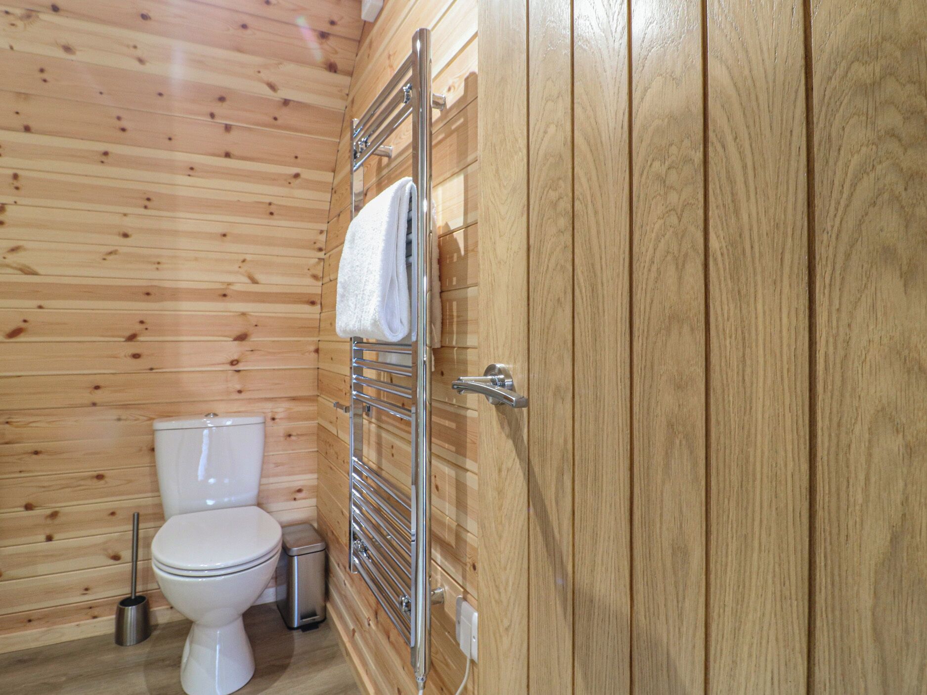 A wooden-paneled bathroom with a toilet, a towel rack, and a trash bin.