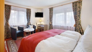 A hotel room with a bed, a desk, a chair, a television, and curtains. - Hotel Bären – Three-Star: Double Room 1 / Breakfast Included / Mountain View / 3 Guests / WiFi (Bernau im Schwarzwald)