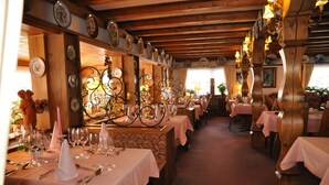 A restaurant with multiple tables set for dining, wooden beams on the ceiling, and wall-mounted plates. - Hotel Bären – Three-Star: Double Room 1 / Breakfast Included / Mountain View / 3 Guests / WiFi (Bernau im Schwarzwald)