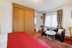 Een kamer met een bed, een houten garderobe, een bank, een klein rond tafeltje en een kamerkleed met dessin.